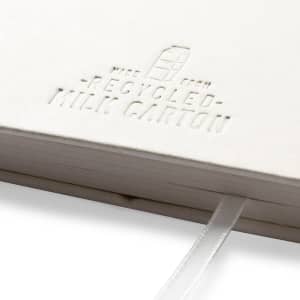 A white notebook with an embossed logo, made from recycled milk cartons, featuring a ribbon bookmark.