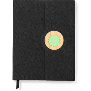 A dark grey notepad with a circular wooden element featuring a green circle. It includes a ribbon bookmark and a logo.