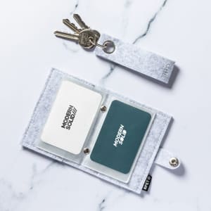 A grey felt business card holder with slots for cards and a keychain attached.