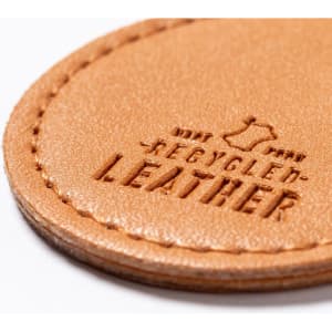 A close-up of a tan keyring made from recycled leather, featuring an embossed logo.