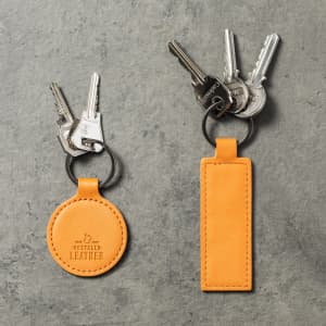An orange leather keyring with a round and a rectangular tag, holding several metal keys.