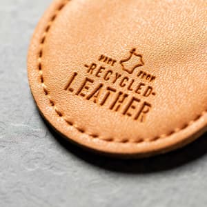 A tan keyring made from recycled leather, featuring embossed lettering.