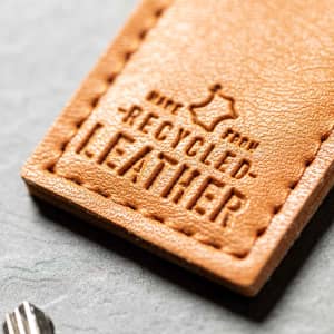 A brown recycled leather tag featuring embossed text, showcasing its eco-friendly material.