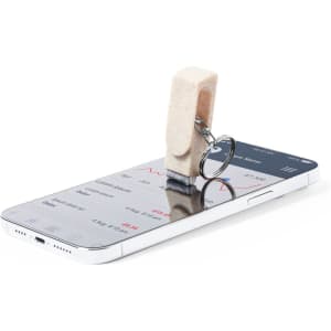 A keyring featuring a beige Peix Holder design, resting on a smartphone displaying a financial app.