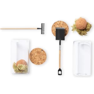 A collection of gardening tools including a rake, shovel, and seed bonbons in glass containers with cork lids, featuring natural colours.