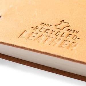 A notebook with a tan recycled leather cover featuring embossed text indicating its material.