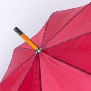 A red umbrella with an orange handle and a silver valve at the top, featuring a logo.