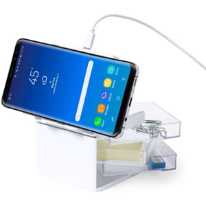 A white organiser with a phone dock, featuring compartments for stationery items and a charging cable connected to a smartphone.