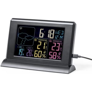 A digital weather station in black displaying time, temperature, humidity, and weather icons, with a charging cable attached.