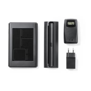 A black weather station set, including a main unit, sensor, battery compartment, and charger. The components are neatly arranged.