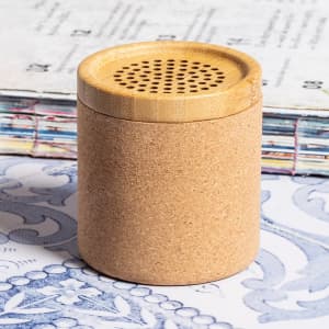 A cylindrical speaker made of cork with a bamboo top, set against a patterned background.