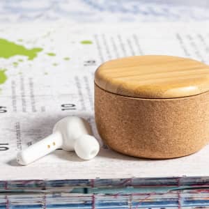 White earphones with a cork base and bamboo lid placed on a textured surface, alongside a green map illustration.