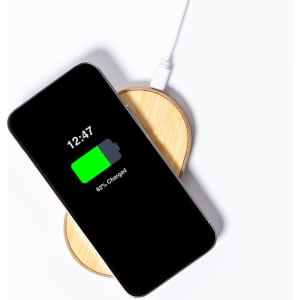 A wireless charger in a circular bamboo design with a smartphone displaying a charging battery indicator.