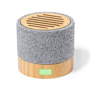 A round speaker features a grey fabric top and a wooden base, with a textured surface and slotted design on top.