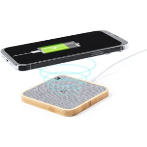 A wireless charger with a wooden base and grey fabric surface, positioned near a smartphone indicating charging.