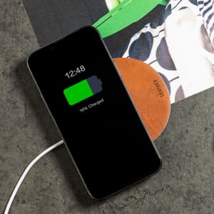 A wireless charger with a leather base and a black smartphone displaying a charging indicator.