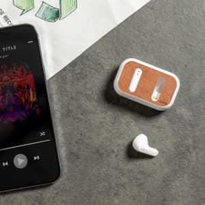 White Shizar RCS earphones alongside a smartphone displaying music, set on a textured surface.