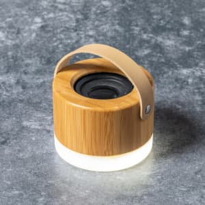 A bamboo speaker with a leather handle and a lit base, set against a textured grey surface.