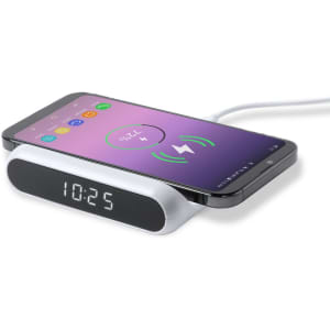 A white multifunction alarm clock with a digital display and a smartphone on top, indicating wireless charging.