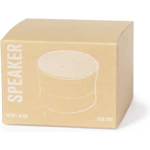 A round black speaker inside a brown cardboard box with a minimalist design and a logo.