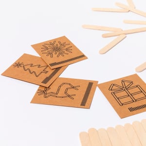 A set of wooden sticks and brown cards featuring outlines of festive designs like a Christmas tree and a gift.