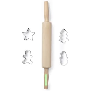A wooden rolling pin with a green handle, accompanied by star, tree, gingerbread man, and snowman cookie cutters.
