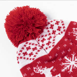 A red and white beanie with a pom-pom on top featuring a festive pattern and a logo.