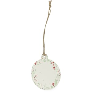A circular Christmas decoration in white, featuring a festive design with green leaves and red berries, hanging by a jute string.