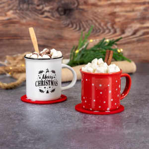 A red and white mug set featuring festive designs and filled with marshmallows, placed on a grey surface.