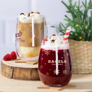 A set of two glass cups, one filled with a creamy beverage, the other with a red drink, both topped with whipped cream.