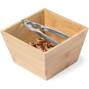 A bamboo box containing a stainless steel nutcracker and nut shells. The box has a square shape.