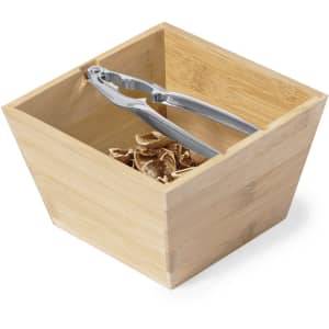 A bamboo container with a metallic nutcracker resting inside, filled with shredded wood.