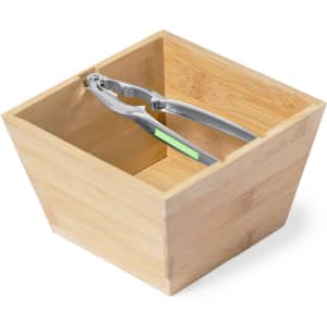 A bamboo nutcracker sits inside a square bamboo container. The container has a natural finish.