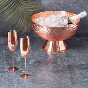 A copper bowl filled with ice and a bottle, alongside two matching copper flute glasses.