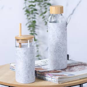 A drink bottle and a glass cup, both with bamboo lids, wrapped in grey felt and placed on a wooden table.