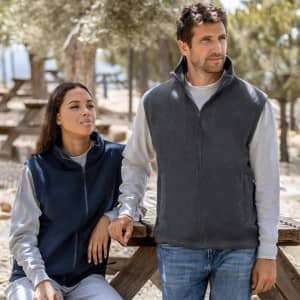A grey vest is worn by a man, alongside a woman in a navy vest, both outdoors in a natural setting.