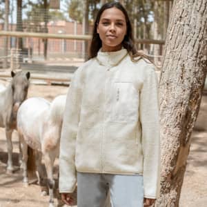A polar fleece jacket in a light cream colour, featuring a zip pocket and a high collar, with a logo present.