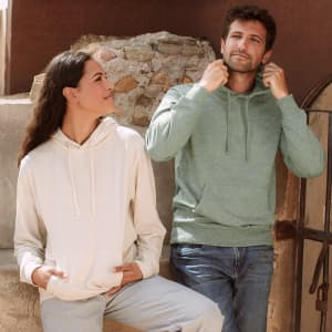 A green hoodie and a cream sweatshirt, both with hoods, styled on a couple against a rustic background.