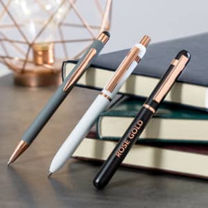 Three stylish stylus touch ball pens in grey, white, and black with rose gold accents, resting on stacked books.