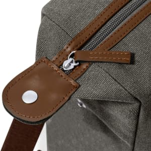 A grey bag with brown leather accents, featuring a zipper and a snap button detail.