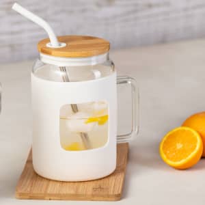 A drink bottle featuring a white exterior, glass body, bamboo lid, and a straw, with citrus fruits nearby.
