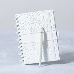 A white notebook with a textured cover and a matching pen. It features a spiral binding and an elastic band.