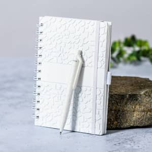 A white notebook with a textured cover, accompanied by a matching pen, displayed on a stone surface.
