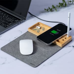 A grey multifunction mousepad with a wooden tray, featuring a phone, a stylus, and office supplies next to a laptop.