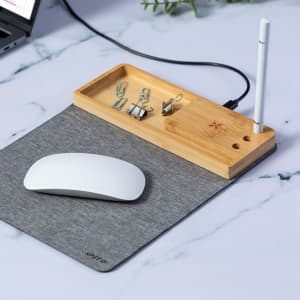 A grey mousepad with a bamboo tray, featuring paperclips and a pen, alongside a white computer mouse.