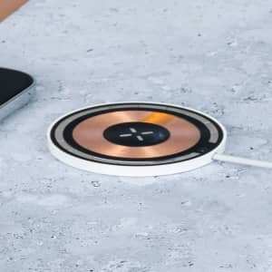 A wireless charger with a circular design featuring a copper surface and a white base, next to a smartphone.