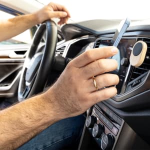 A car phone holder in use, featuring wooden accents, securely mounted on a car dashboard with a smartphone being placed.