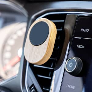 A bamboo car phone holder with a circular black surface, mounted on a car air vent.