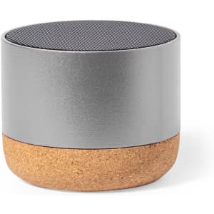A compact speaker with a silver top and cork base, featuring a sleek, minimalist design and a logo.
