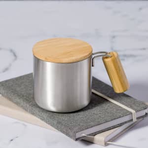 A silver insulated mug with a wooden lid and handle, resting on top of two grey notebooks.